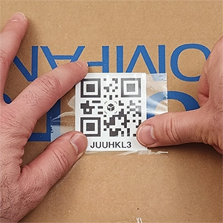 Hand applying a printed QR code with transparent tape to a cardboard storage box